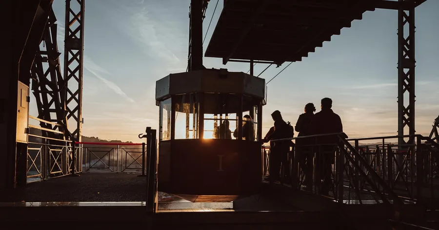 Siluetas de personas esperando junto a una cabina del teleférico en una estación en lo alto, al atardecer