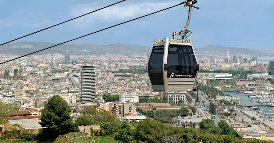 Una cabina del teleférico de Montjuïc sobrevolando la ciudad, con el puerto y sus grúas a la derecha