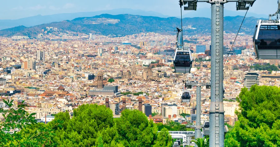Cabinas del teleférico y una torre sobre pinos verdes, con toda Barcelona y la sierra de Collserola al fondo