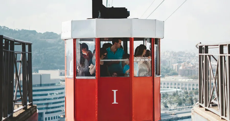 Una cabina roja de época del Teleférico del Puerto en su estación, con la ciudad extendida al fondo